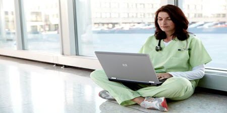 Klinický lekár sediaci na podlahe a čítajúci notebook 
